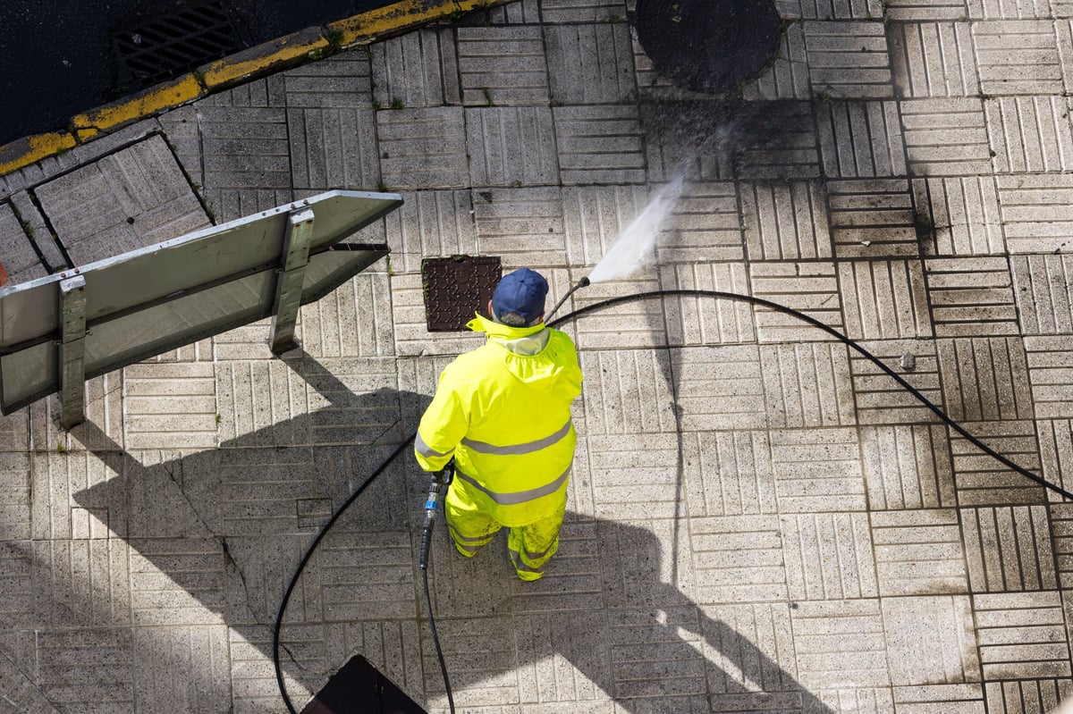 Worker cleaning exterior paving with a high pressure water jet