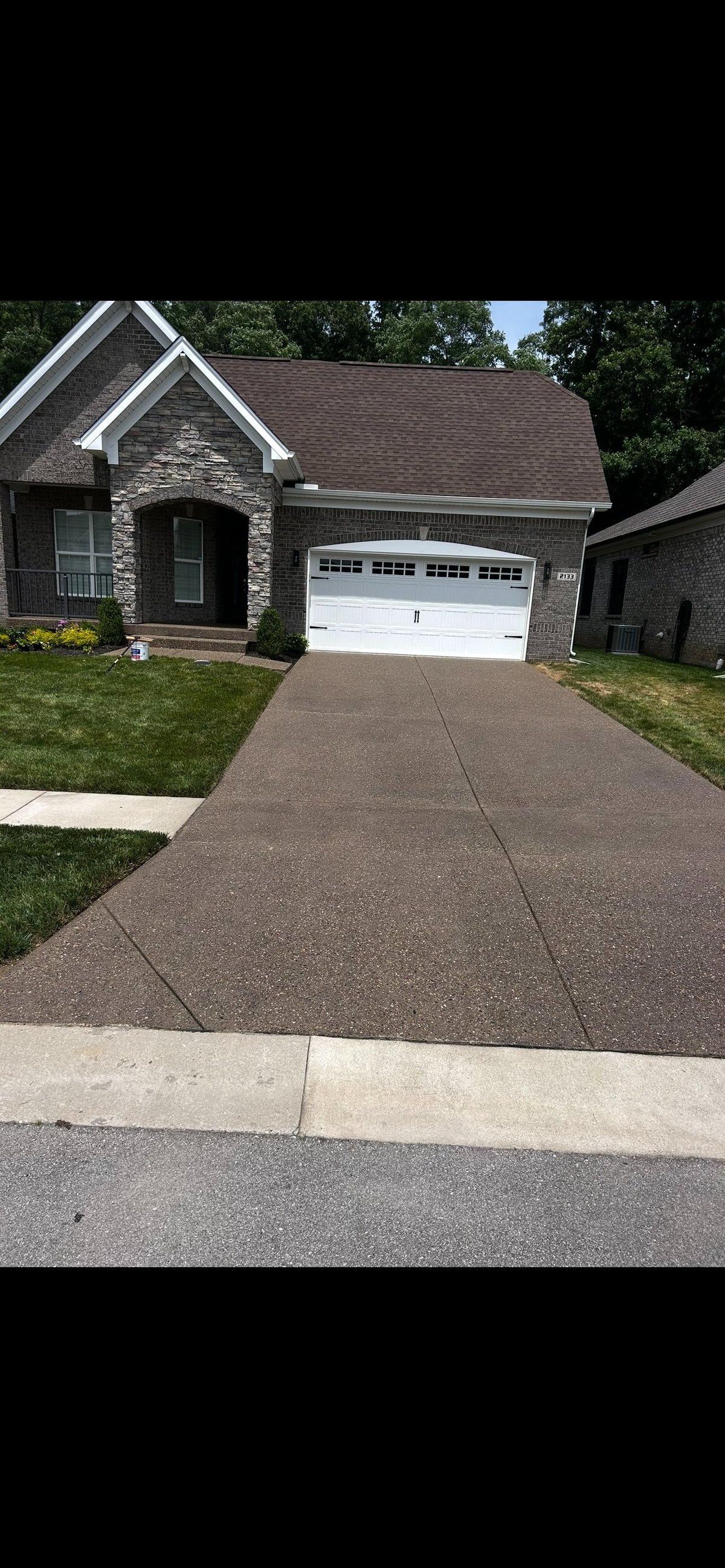 Modern brick and stone single-family home with white two-car garage, manicured lawn, and dark asphalt driveway